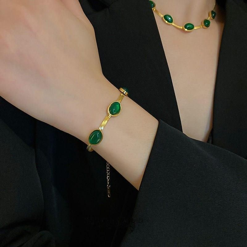 Gold bracelet with green stones on a wrist, worn by a person in a black outfit.